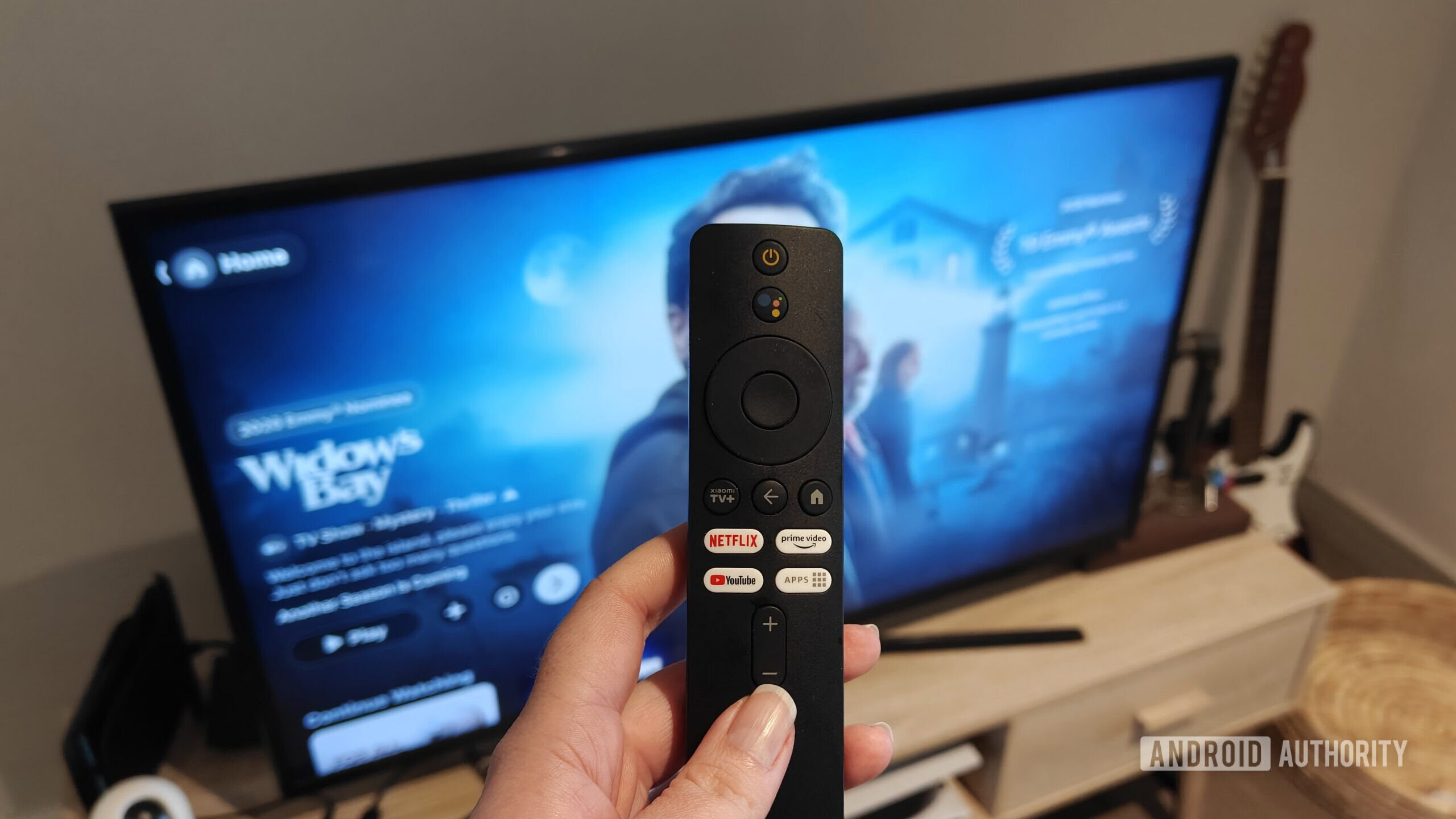 A remote held in front of a TV with the Apple TV app in the background